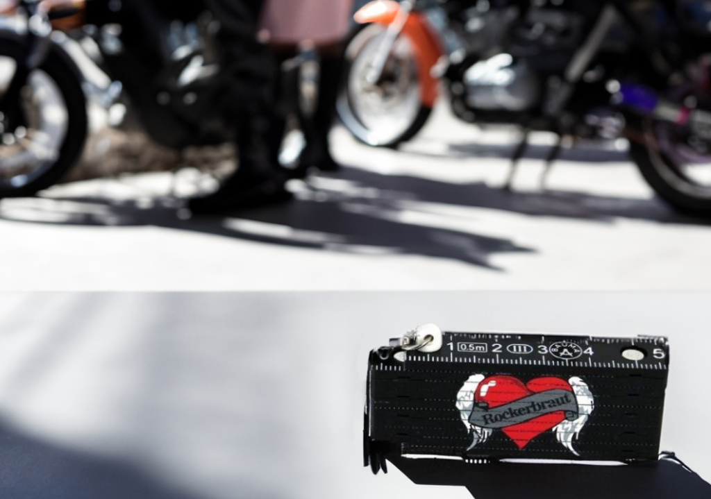 Kleiner bedruckter Zollstock Herz und mit Aufschrift 'Rockerbraut'. Im Hintergrund Motorräder.
